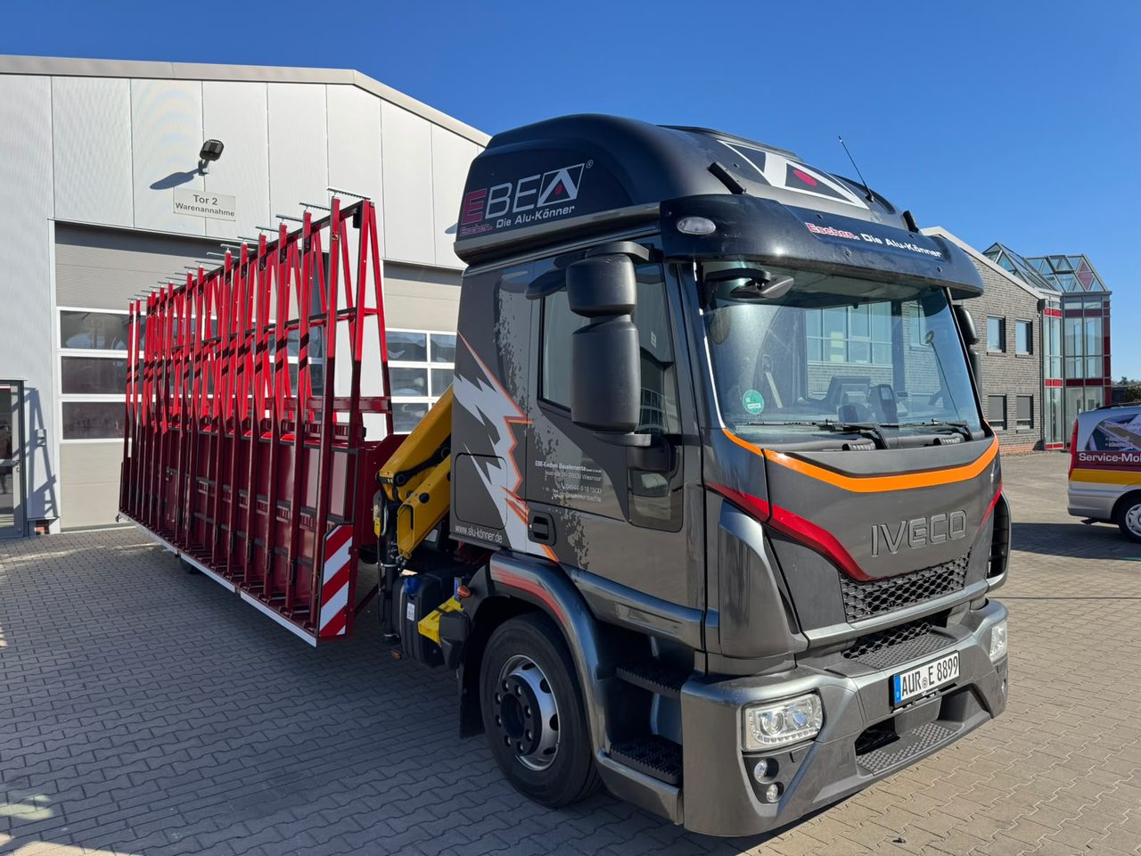 EBE-Lkw mit Ladekran und rotem Glasgestell vor einer Halle