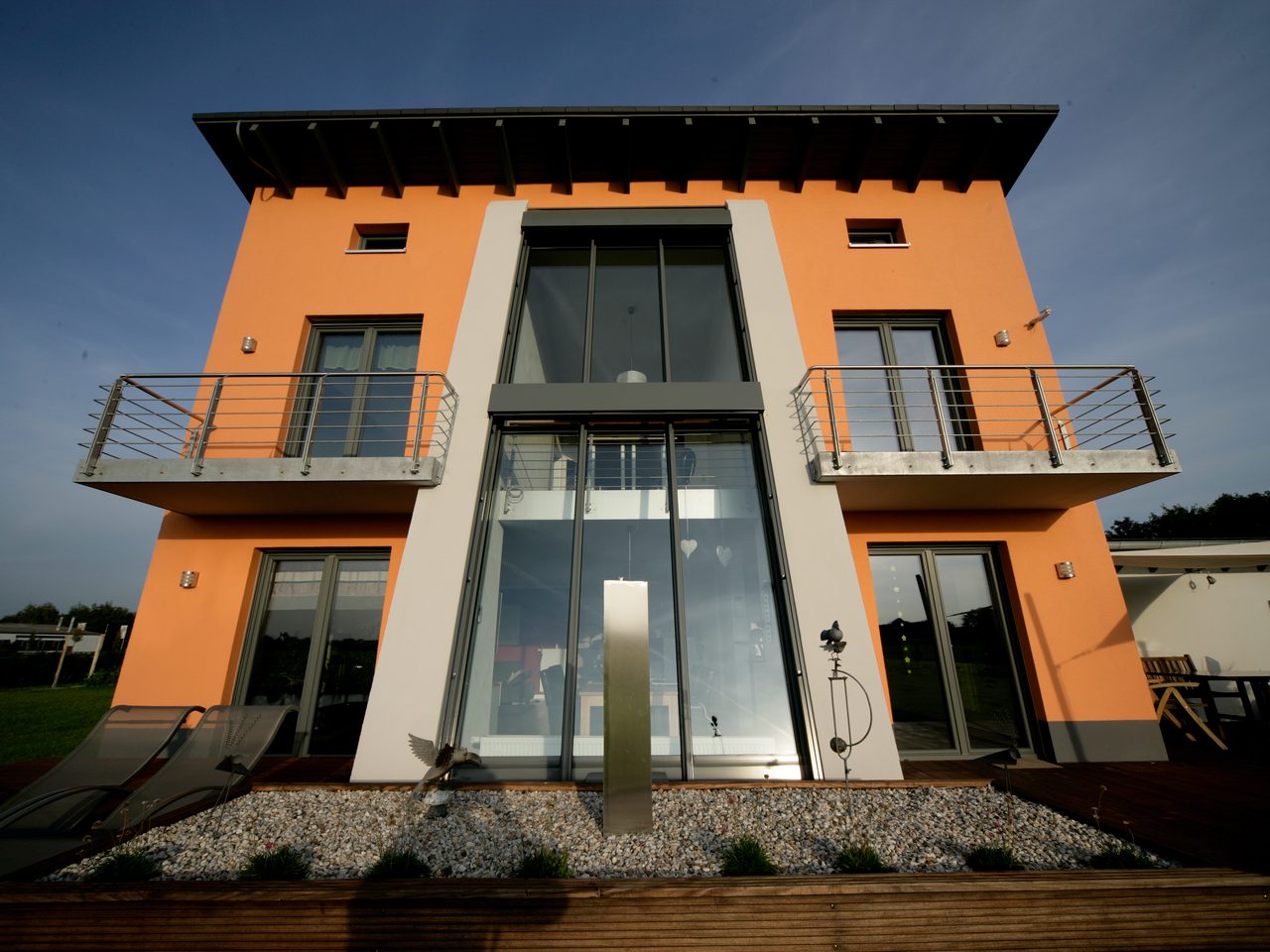 Zweigeschossiges Glaselement in der Fassade eines orangefarbenen Wohnhauses im Abendlicht