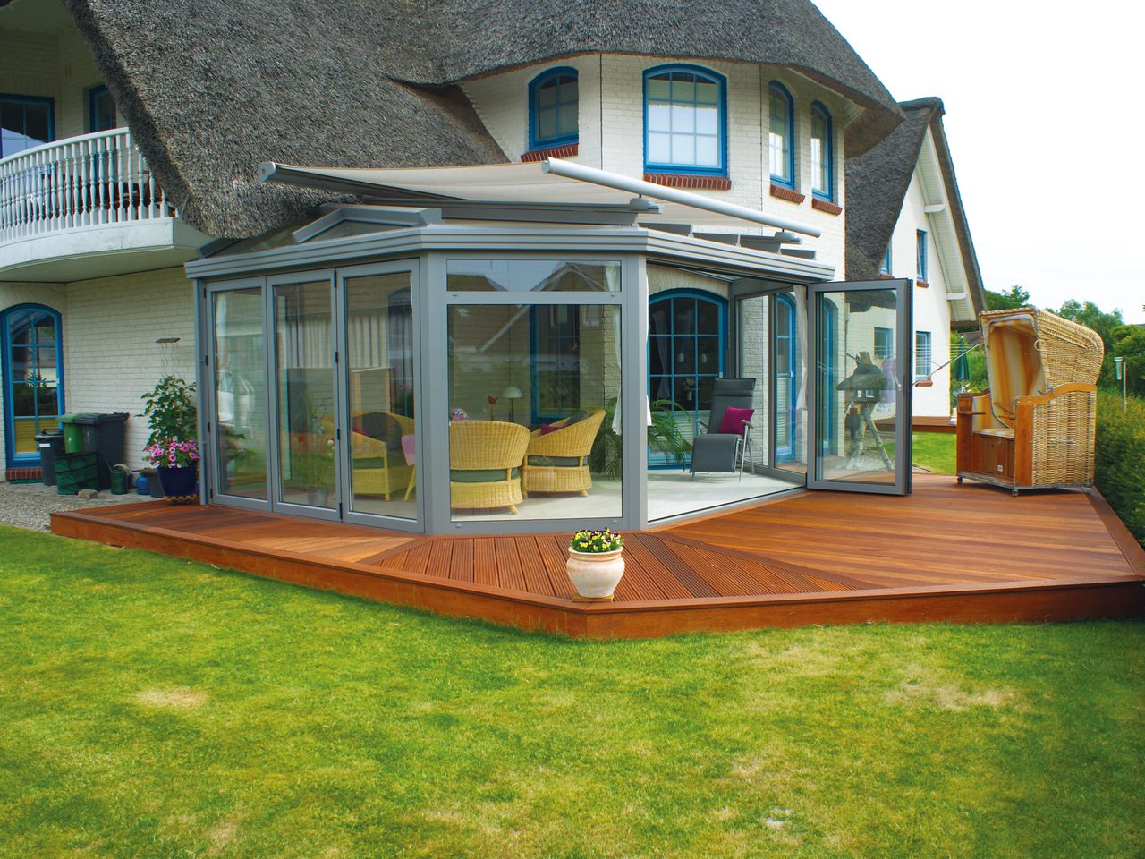 Wintergarten mit geöffneter Faltanlage auf einer Holzterrasse vor einem reetgedeckten Haus