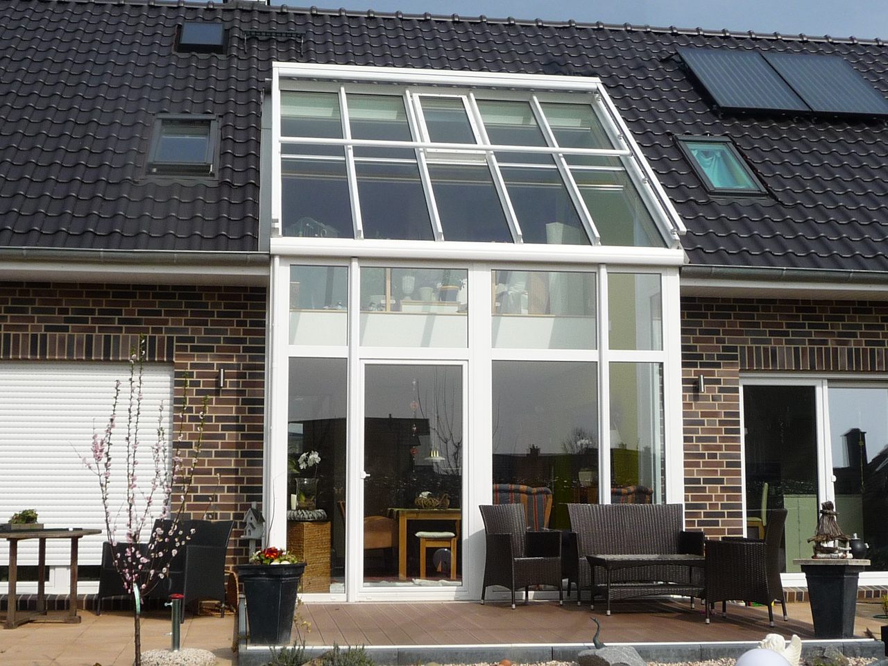 Weißer Glasgiebel mit Glasdach, eingebunden in das Ziegeldach eines Klinkerhauses